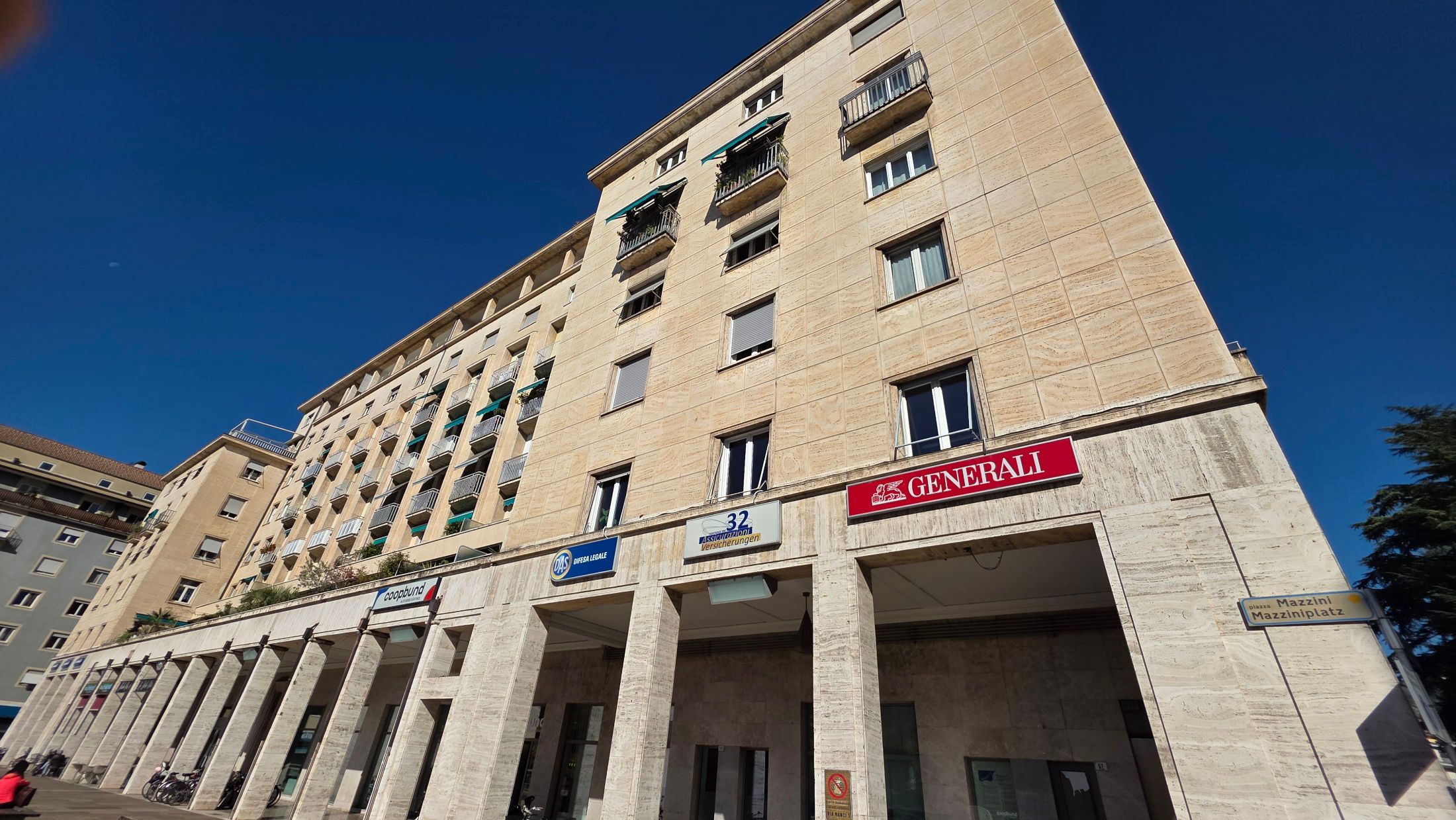 Il palazzo di Via Manci 5 a Bolzano con i portici in travertino e le insegne di Generali, Trentadue Assicurazioni e DAS